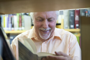 Porträt eines lächelnden älteren Mannes in einer Stadtbibliothek, der ein Buch liest - FRF00572