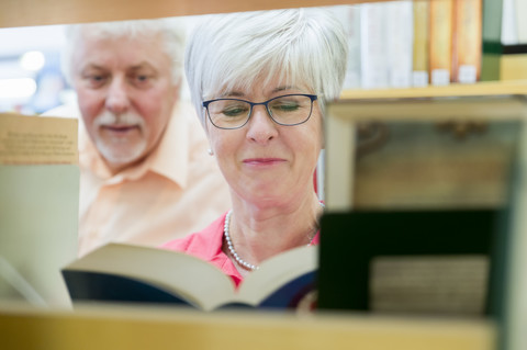 Portrait of smiling senior woman with book in a city library stock photo