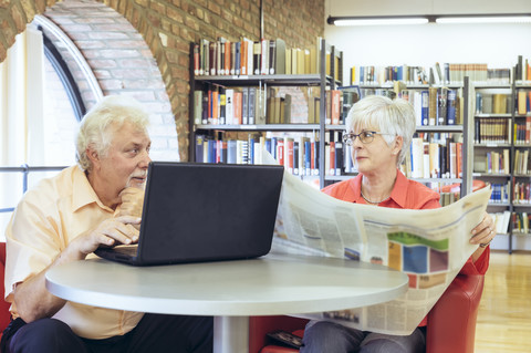 Älteres Paar mit Laptop und Zeitung in einer Stadtbibliothek, lizenzfreies Stockfoto