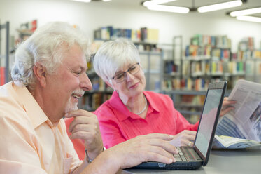 Senior couple with laptop and newspaper in a city library - FRF00577