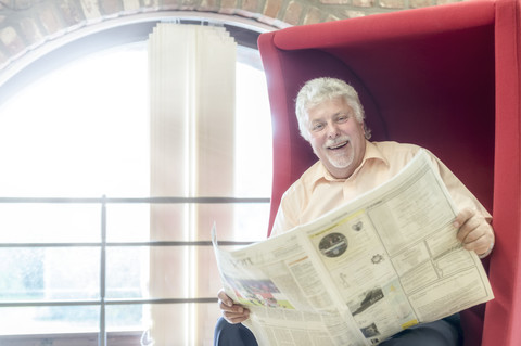 Porträt eines glücklichen älteren Mannes mit Zeitung in einer Stadtbibliothek, lizenzfreies Stockfoto