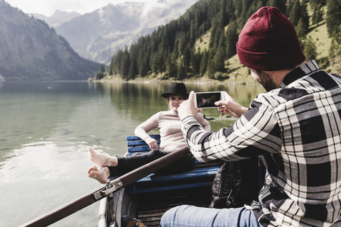 Österreich, Tirol, Alpen, Mann macht Handyfoto von Frau in Ruderboot auf Bergsee, lizenzfreies Stockfoto