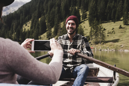 Österreich, Tirol, Alpen, Frau macht Handyfoto von lächelndem Mann in Ruderboot auf Bergsee - UUF11960