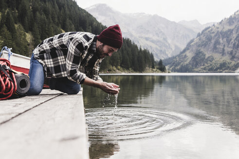 Österreich, Tirol, Alpen, Mann kniend auf Steg schöpft Wasser aus Bergsee - UUF11972