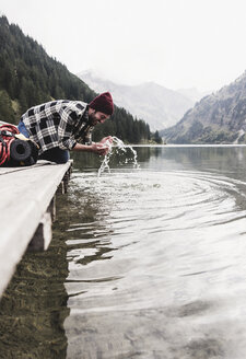 Österreich, Tirol, Alpen, Mann kniend auf Steg erfrischend am Bergsee - UUF11974