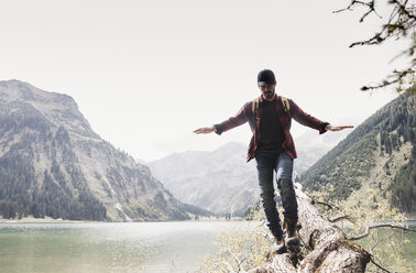 Austria, Tyrol, Alps, hiker balancing on tree trunk at mountain lake - UUF11990