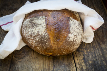 In ein Küchentuch eingewickeltes Weizenbrot auf dunklem Holz - LVF06349