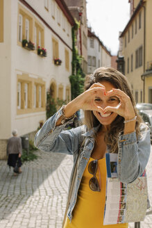 Deutschland, Rothenburg ob der Tauber, Porträt einer glücklichen Frau, die mit ihren Fingern ein Herz formt - MOMF00268