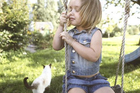 Kleines Mädchen sitzt auf einer Schaukel im Garten, lizenzfreies Stockfoto