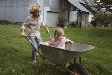 Boy pushing wheelbarrow with his little sister through the garden - KMKF00027