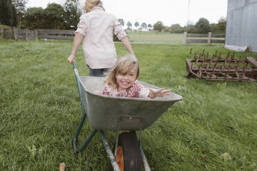Boy pulling wheelbarrow with his little sister through the garden - KMKF00028