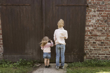 Rückansicht des Bruders und seiner kleinen Schwester vor einer Holztür - KMKF00029