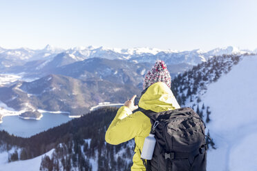 Germany, Bavaria, Alps, hiker with backpack at Lake Walchen taking smartphone picture - MMAF00147