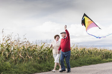 Glückliches Seniorenpaar mit Drachen in ländlicher Landschaft - UUF12002