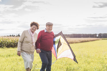 Glückliches älteres Paar, das mit einem Drachen in einer ländlichen Landschaft spazieren geht - UUF12011