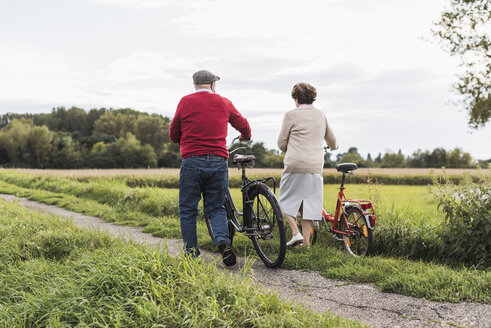 Älteres Paar schiebt Fahrräder in ländlicher Landschaft - UUF12012