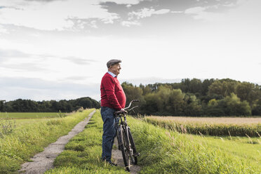 Älterer Mann mit Fahrrad in ländlicher Landschaft - UUF12013