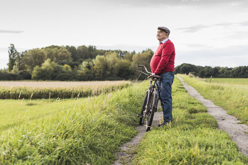 Älterer Mann mit Fahrrad in ländlicher Landschaft - UUF12014