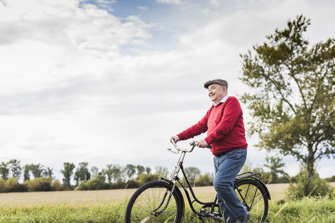 Älterer Mann schiebt Fahrrad in ländlicher Landschaft, lizenzfreies Stockfoto