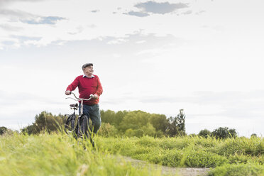 Älterer Mann schiebt Fahrrad in ländlicher Landschaft - UUF12018