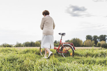 Ältere Frau schiebt Fahrrad in ländlicher Landschaft - UUF12022