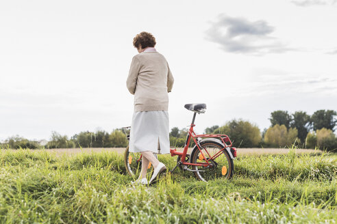 Ältere Frau schiebt Fahrrad in ländlicher Landschaft - UUF12022