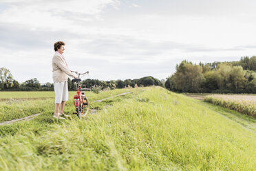 Ältere Frau mit Fahrrad in ländlicher Landschaft - UUF12023