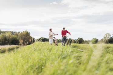 Senior couple pushing bicycles in rural landscape - UUF12025