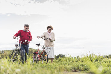 Senior couple pushing bicycles in rural landscape - UUF12028