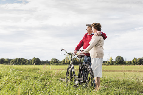 Älteres Paar mit Fahrrädern, die sich in ländlicher Landschaft umarmen, lizenzfreies Stockfoto