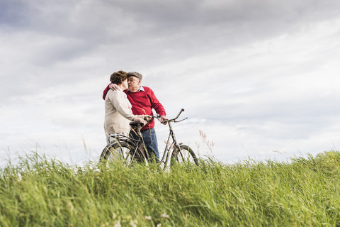 Älteres Paar mit Fahrrädern, das sich in einer ländlichen Landschaft küsst, lizenzfreies Stockfoto