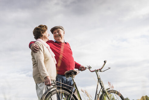 Glückliches älteres Paar mit Fahrrädern, das sich umarmt - UUF12034