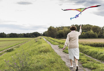 Senior woman walking with kite in rural landscape - UUF12042