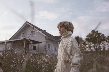 Boy standing in field beside rural house - KMKF00033