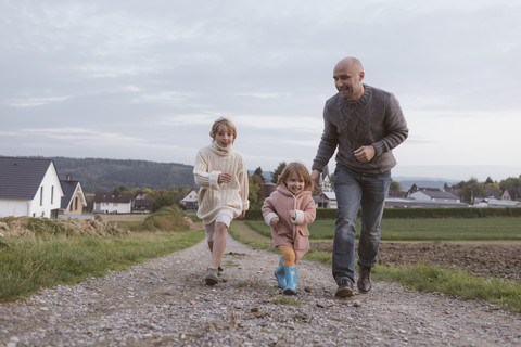 Vater mit zwei Kindern läuft auf einem Feldweg, lizenzfreies Stockfoto