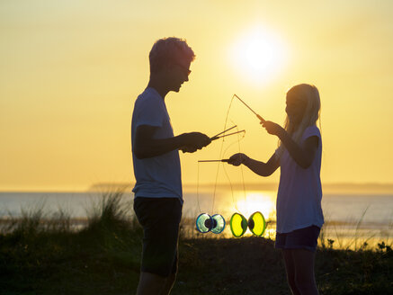 Frankreich, Bretagne, Sainte-Anne-la-Palud, La Plage de Treguer, Bruder und Schwester jonglieren mit Diabolo bei Sonnenuntergang - LAF01923