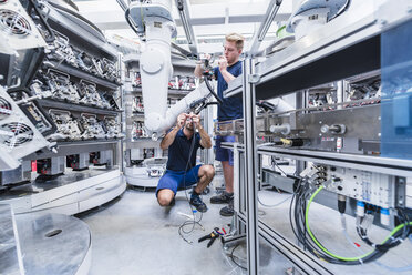Zwei Kollegen arbeiten an einem Industrieroboter in einer modernen Fabrik - DIGF02937