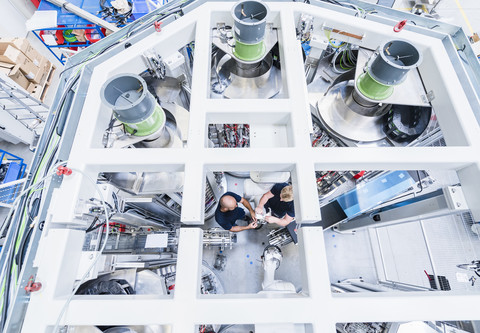 Draufsicht auf zwei Kollegen, die in einer modernen Fabrik an einem Industrieroboter arbeiten, lizenzfreies Stockfoto