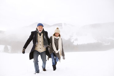 Portrait of happy senior couple walking in snow-covered landscape - HAPF02228
