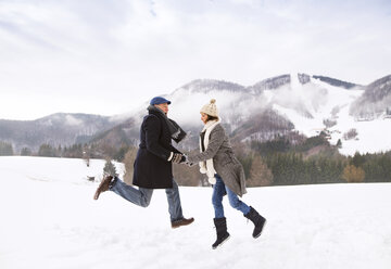 Glückliches älteres Paar, das in einer verschneiten Landschaft in die Luft springt - HAPF02231