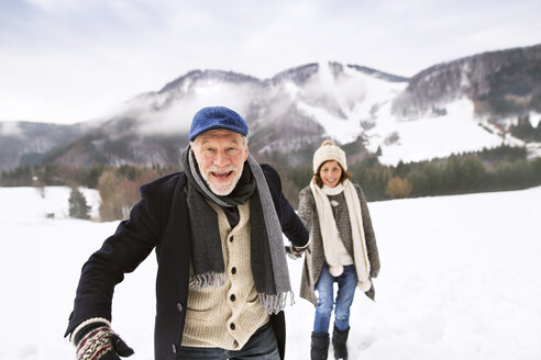 Porträt eines älteren Mannes, der Hand in Hand mit seiner Frau in einer verschneiten Landschaft spazieren geht - HAPF02232