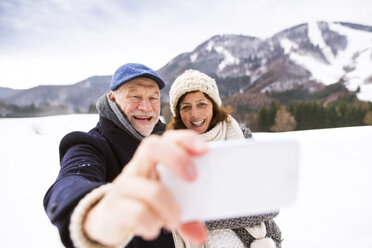 Älteres Paar, das sich küsst und ein Selfie mit dem Handy in einer Winterlandschaft macht - HAPF02236