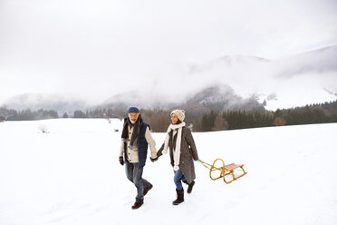 Happy senior couple with sledge walking in snow-covered landscape - HAPF02245