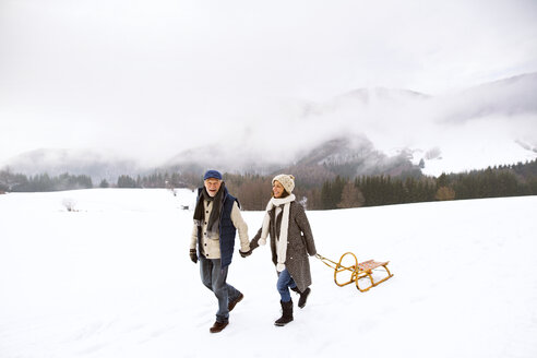 Glückliches Seniorenpaar mit Schlitten in verschneiter Landschaft - HAPF02245