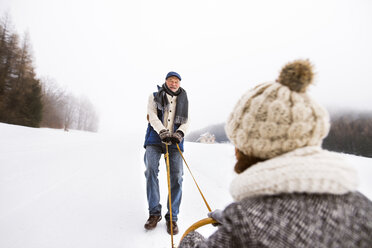 Glückliches älteres Paar hat Spaß mit Schlitten in schneebedeckter Landschaft - HAPF02249