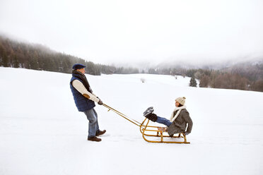 Senior couple having fun with sledge in snow-covered landscape - HAPF02250