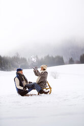 Älteres Paar mit Schlitten, das sich in einer verschneiten Landschaft amüsiert - HAPF02256