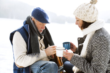 Senior couple having a break with hot beverages in snow - HAPF02257