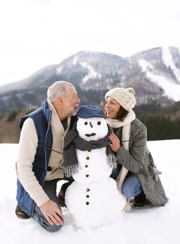 Älteres Paar mit Schneemann in Winterlandschaft, lizenzfreies Stockfoto