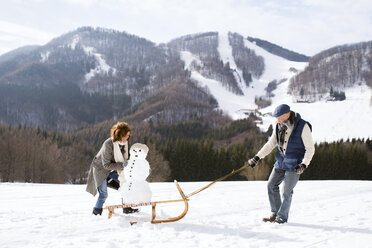 Senior couple with snowman on sledge in winter landscape - HAPF02272